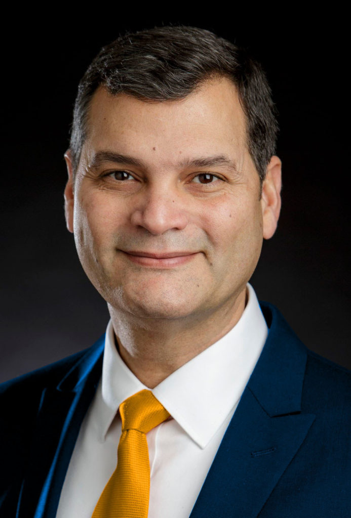 Dr. Atiles smiles at the camera for a professional headshot. He is wearing a blue suit with a yellow tie.