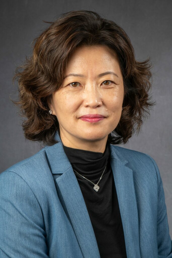 Dr. Kim smiles at the camera wearing a light blue blazer over a black blouse.